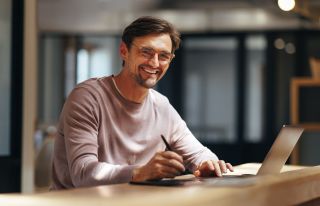 Witte man met bril lachend achter laptop