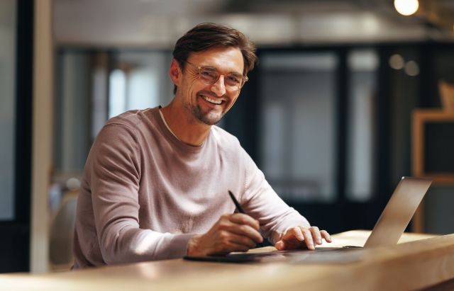 Witte man met bril lachend achter laptop