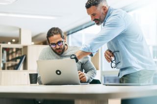 Man met grijze baard geeft uitleg aan witte man met donker haar