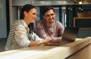 Vrouw met donkerblond haar werkt samen met man met bril achter laptop